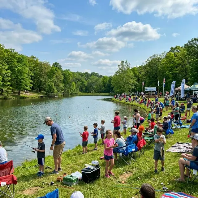 Children participating in a fishing derby event at a Missouri community lake with families gathered on the grassy bank